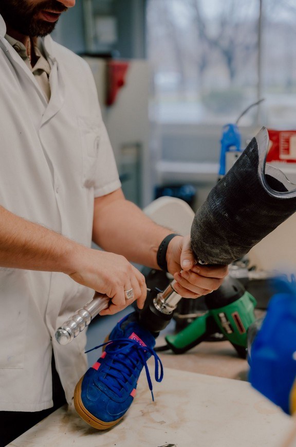 Un prothésiste de l'INI ajuste à la clé le pied et le tube d'une prothèse de jambe à emboîture carbone, chaussée d'une basket, dans l'atelier d'appareillage