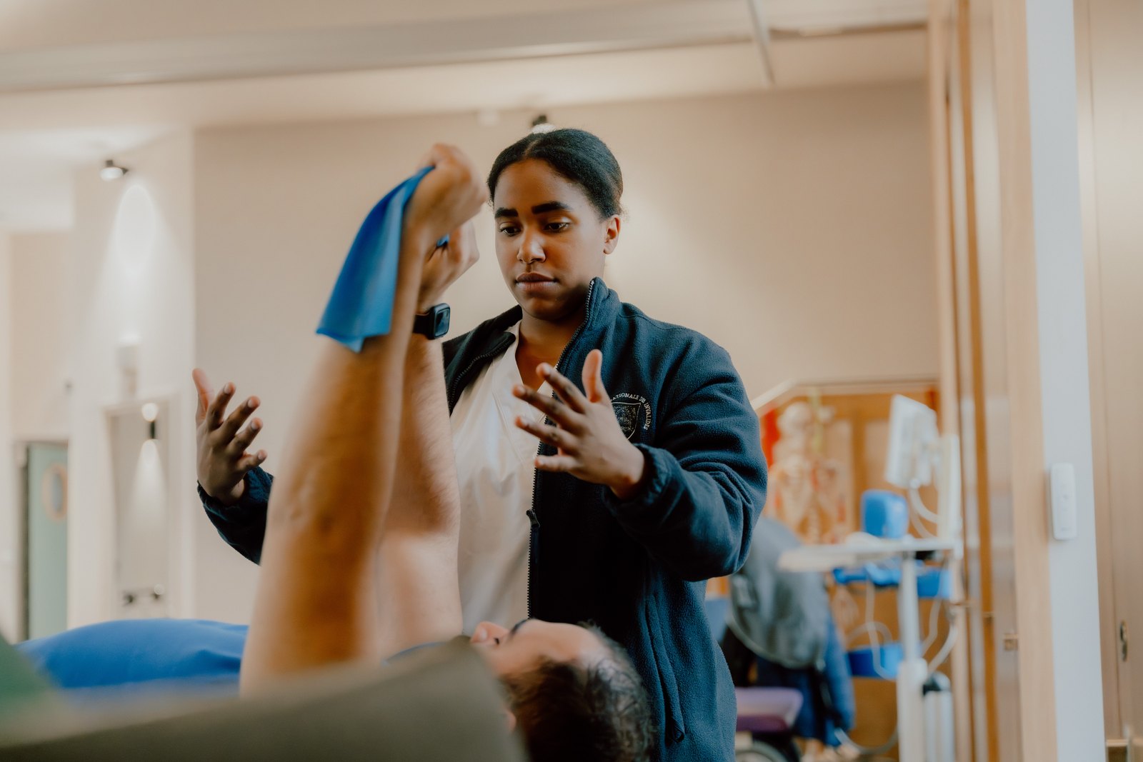 Une soignante du CRPT guide un patient dans un exercice de rééducation du membre supérieur avec bande élastique, dans la salle de réhabilitation