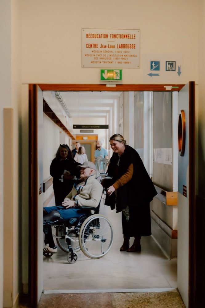 Une soignante accueille en souriant un patient en fauteuil à l'entrée du centre