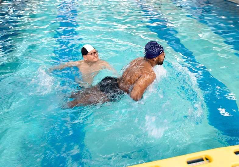 Dans le bassin de balnéothérapie de l'INI, un soignant accompagne un pensionnaire lors d'un exercice de nage