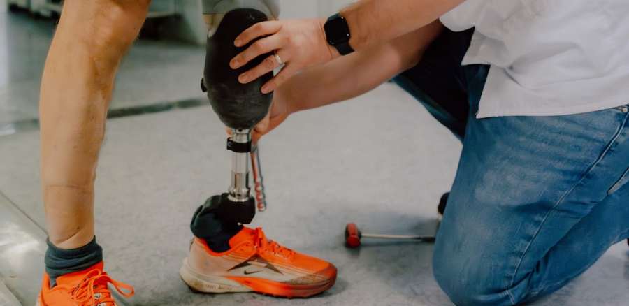 Un prothésiste de l'INI règle la prothèse de jambe d'un patient chaussé de baskets de course, dans l'atelier d'appareillage