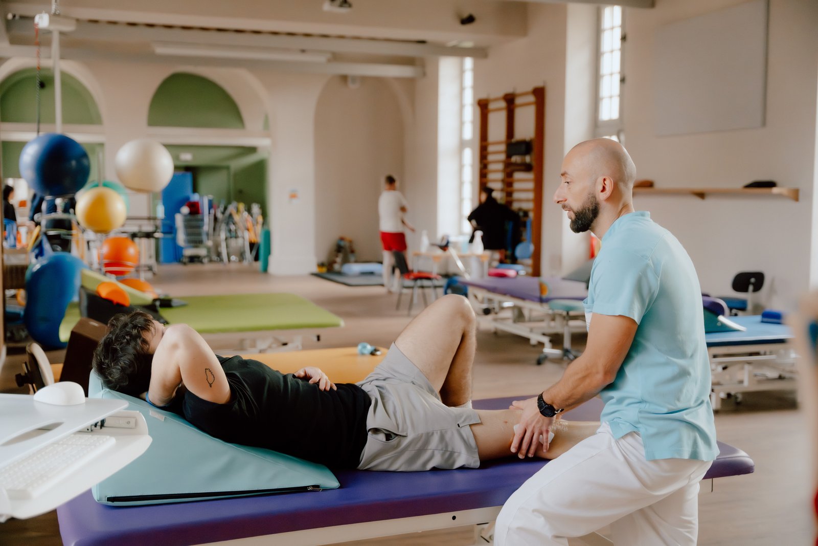 Un kinésithérapeute de l'INI mobilise la jambe d'un patient allongé sur une table de rééducation, dans la salle de réhabilitation