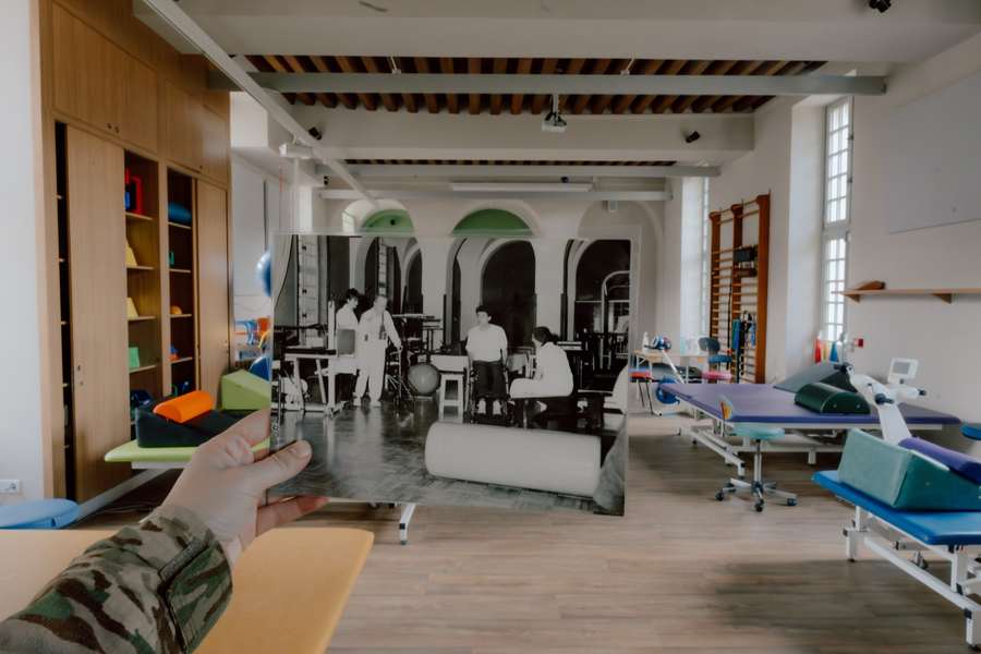 Une main tient une photographie en noir et blanc de l'ancienne salle de rééducation de l'INI, superposée à la salle de rééducation actuelle