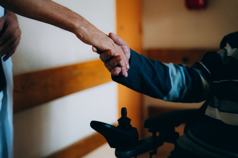 Poignée de main réconfortante entre un soignant et un patient en fauteuil
