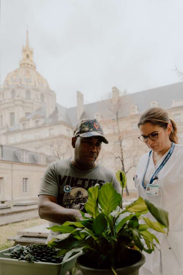 Un pensionnaire jardine avec une soignante, le dôme doré des Invalides en arrière-plan