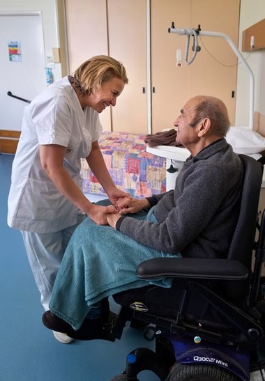 Une soignante tient chaleureusement les mains d'un pensionnaire en fauteuil roulant dans sa chambre