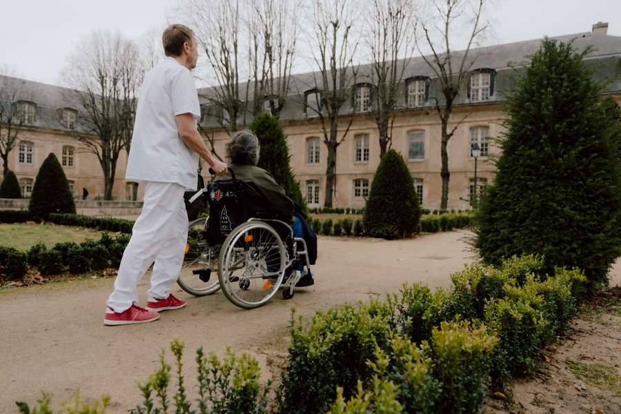 Un soignant accompagne un pensionnaire en fauteuil dans les jardins de l'INI