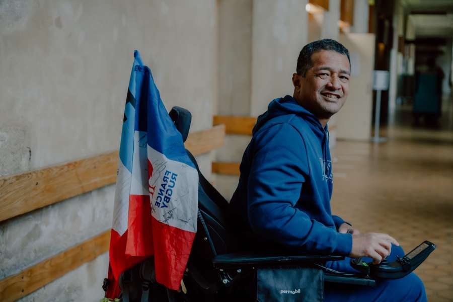 Un pensionnaire souriant en fauteuil roulant, le drapeau tricolore du XV de France accroché à son fauteuil